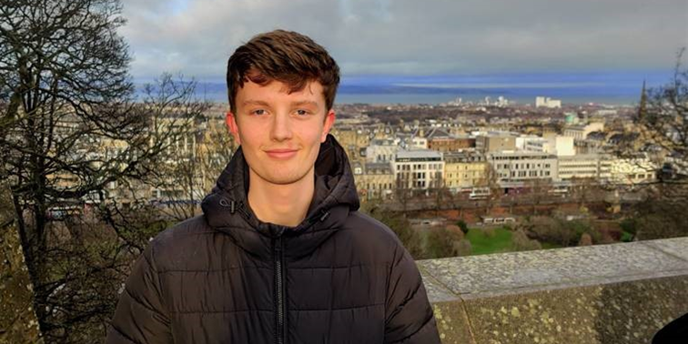 Student standing with a town and the seaside in the background.